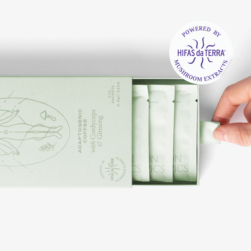 Slightly opened box of Mojo Cordyceps and Ginseng adaptogenic coffee showing three single serve sachets. A hand pull the box open. In the top right corner is a sticker that reads: Powered by Hifas da Terra mushroom extracts.