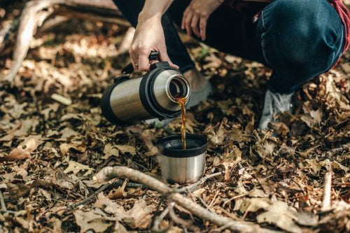 Person pouring dragons den coffee from a flask in the wilderness