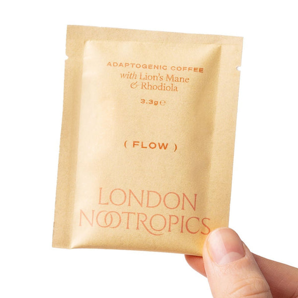Hand holding a single-serve orange sachet of London Nootropics Flow  adaptogenic coffee which features Lion's Mane and Rhodiola.