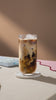 A table with an iced coffee in the foreground while London Nootropics boxes with adaptogenic coffee blends are changing in the background.